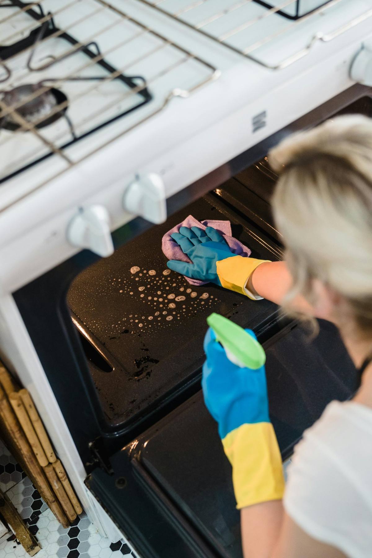 Professional cleaner scrubbing oven with gloves and spray